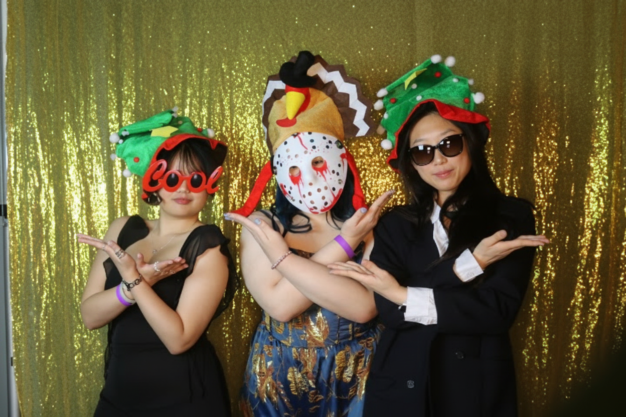 Three guests in costume props striking a pose in front of the gold sequin backdrop